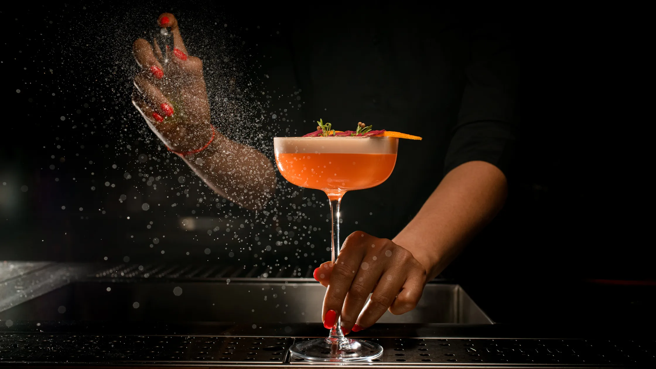 A bartender skillfully garnishing a cocktail with a citrus twist and a sprig of mint